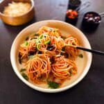 Pasta cooked and coiled into nests on a plate with basil.