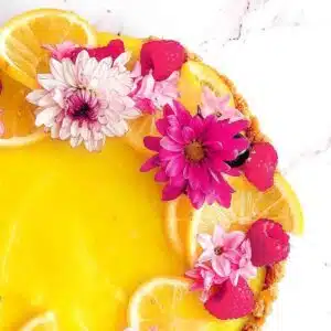 Lemon tart decorated with lemons, raspberries and flowers.
