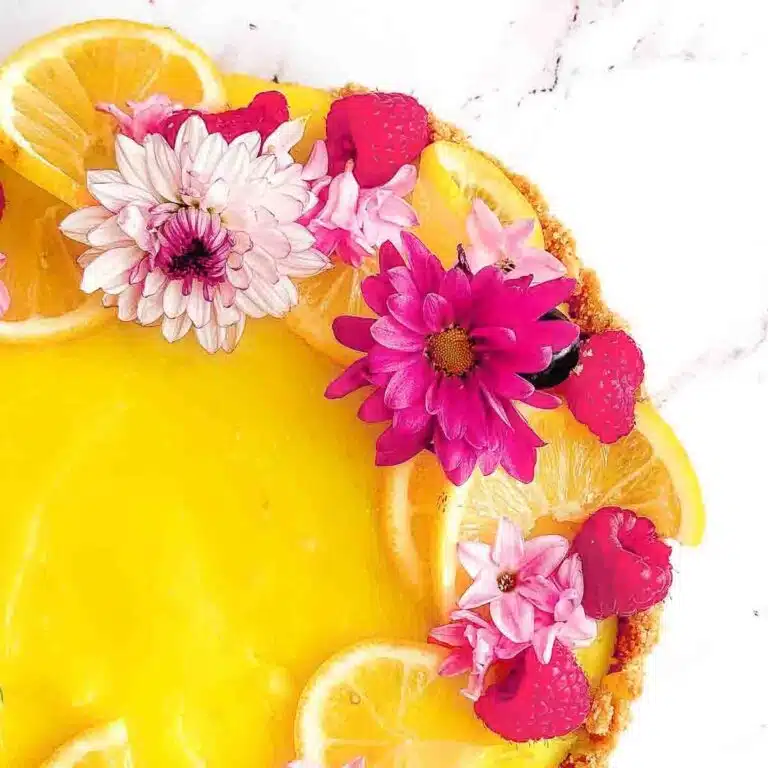 Lemon tart decorated with lemons, raspberries and flowers.