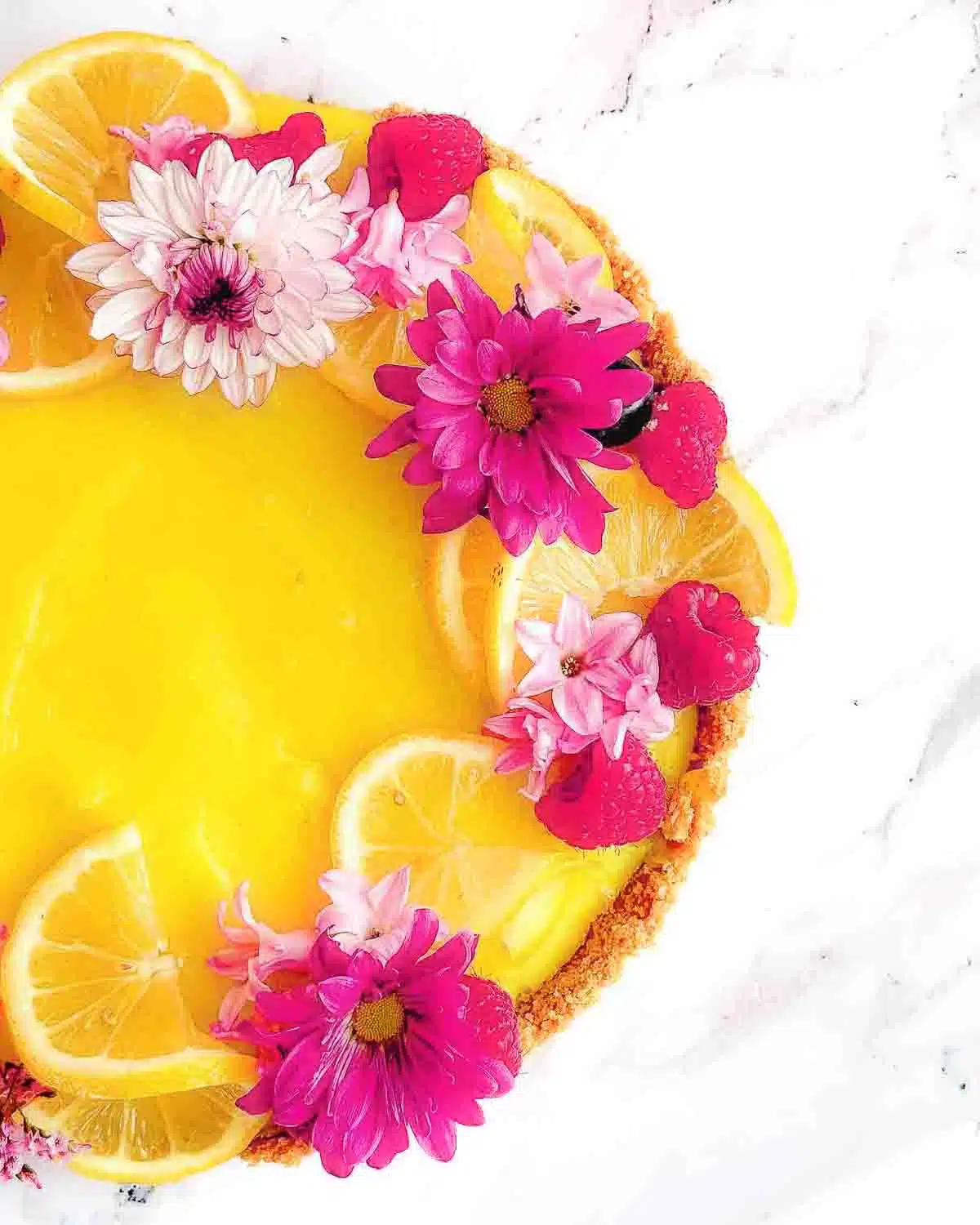 Lemon tart decorated with lemons, raspberries and flowers.