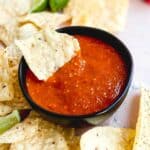 Chip resting in a bowl of spicy red tomatillo salsa.