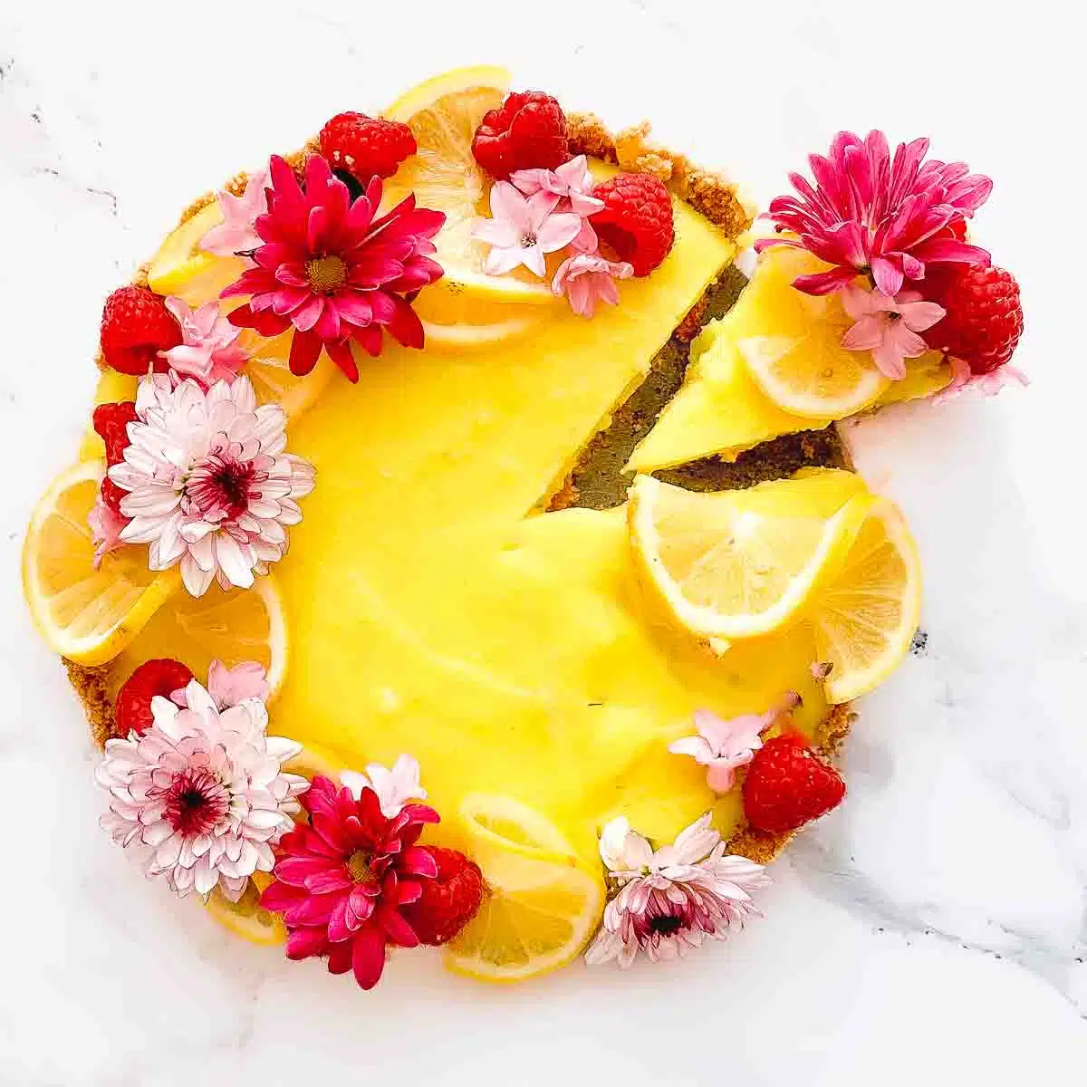 Lemon tart decorated with lemons, raspberries and flowers.
