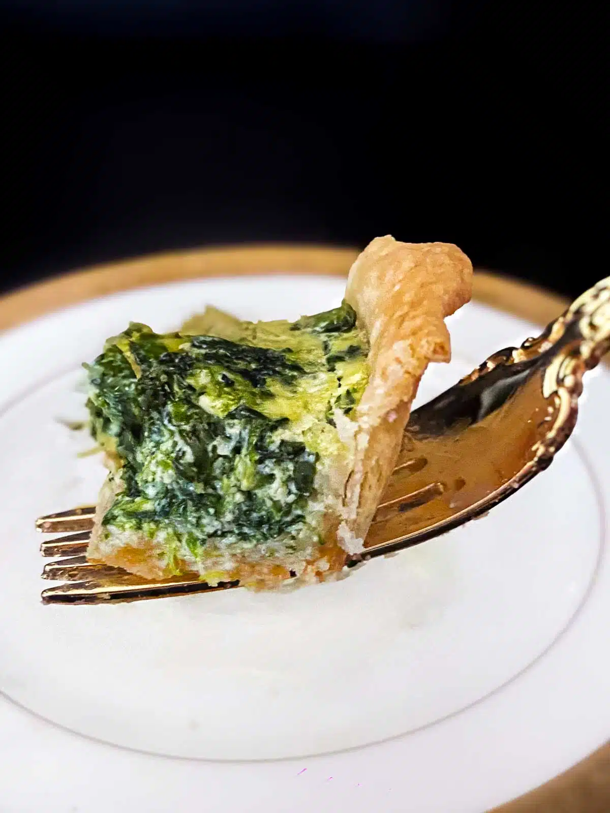 One bite of spinach quiche resting on a gold fork. 