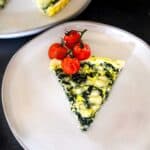 Slice of spinach quiche on a plate with roasted tomatoes.