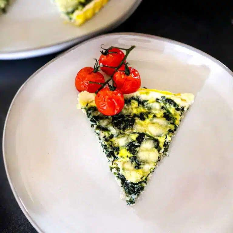 Slice of spinach quiche on a plate with roasted tomatoes.