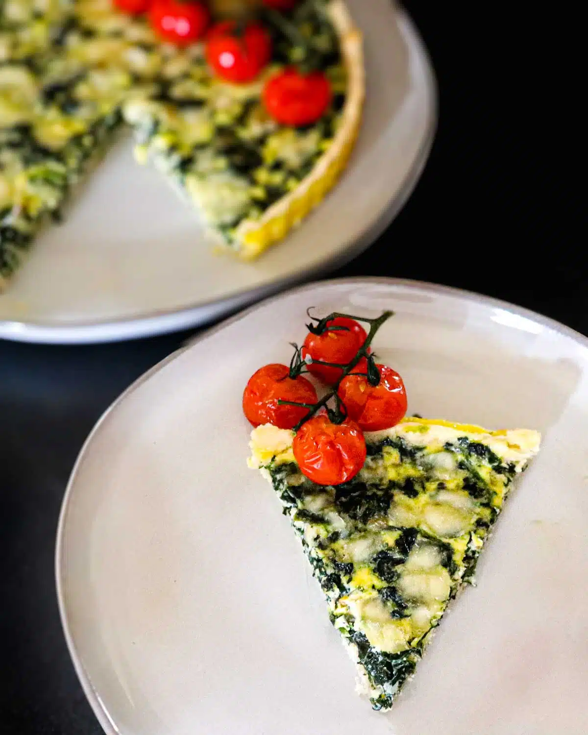 Slice of spinach quiche on a plate with roasted cherry tomatoes. 