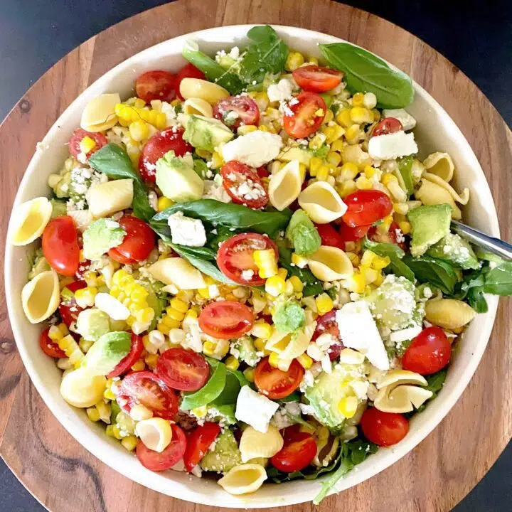 A top down view of corn avocado salad.  Salad has lots of tomatoes, corn, garbanzo bean pasta shells, and basil. 