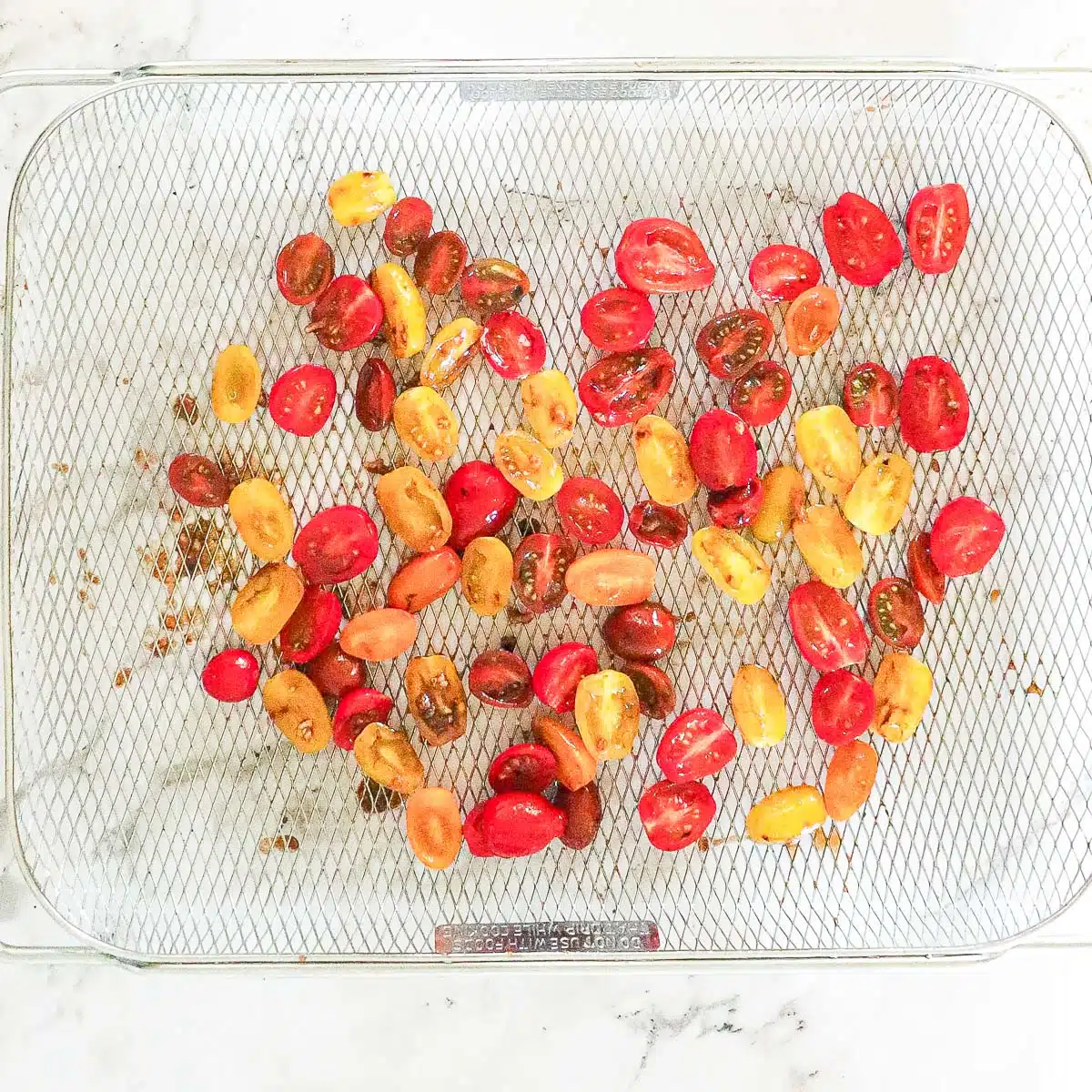 Tomatoes halved and on an air fryer basket.