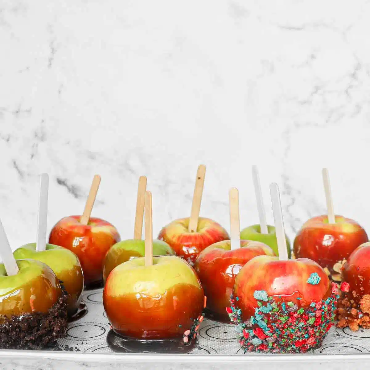 Several caramel apples drying on a tray.