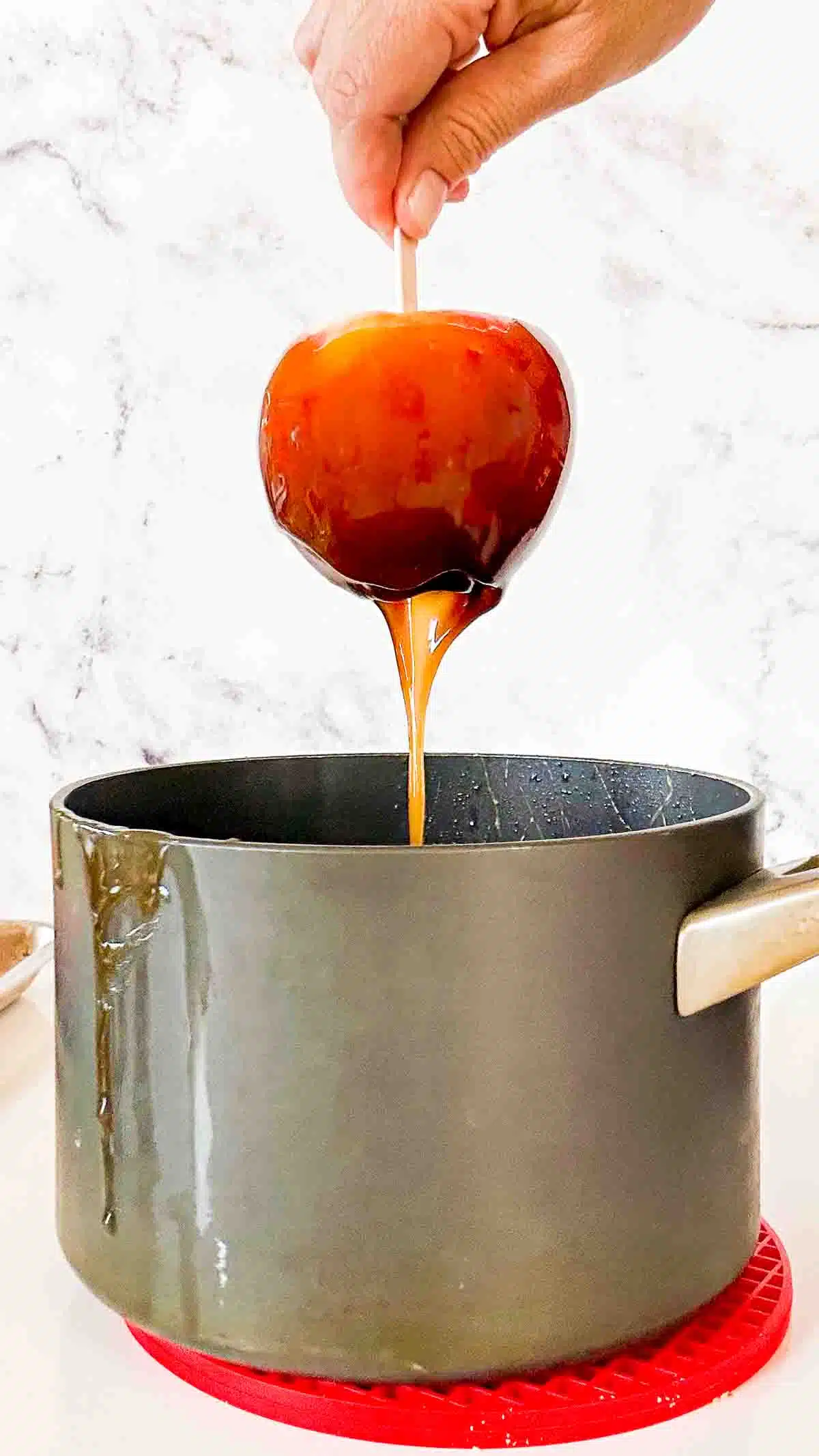 Caramel dripping off an aple into a soucepan.