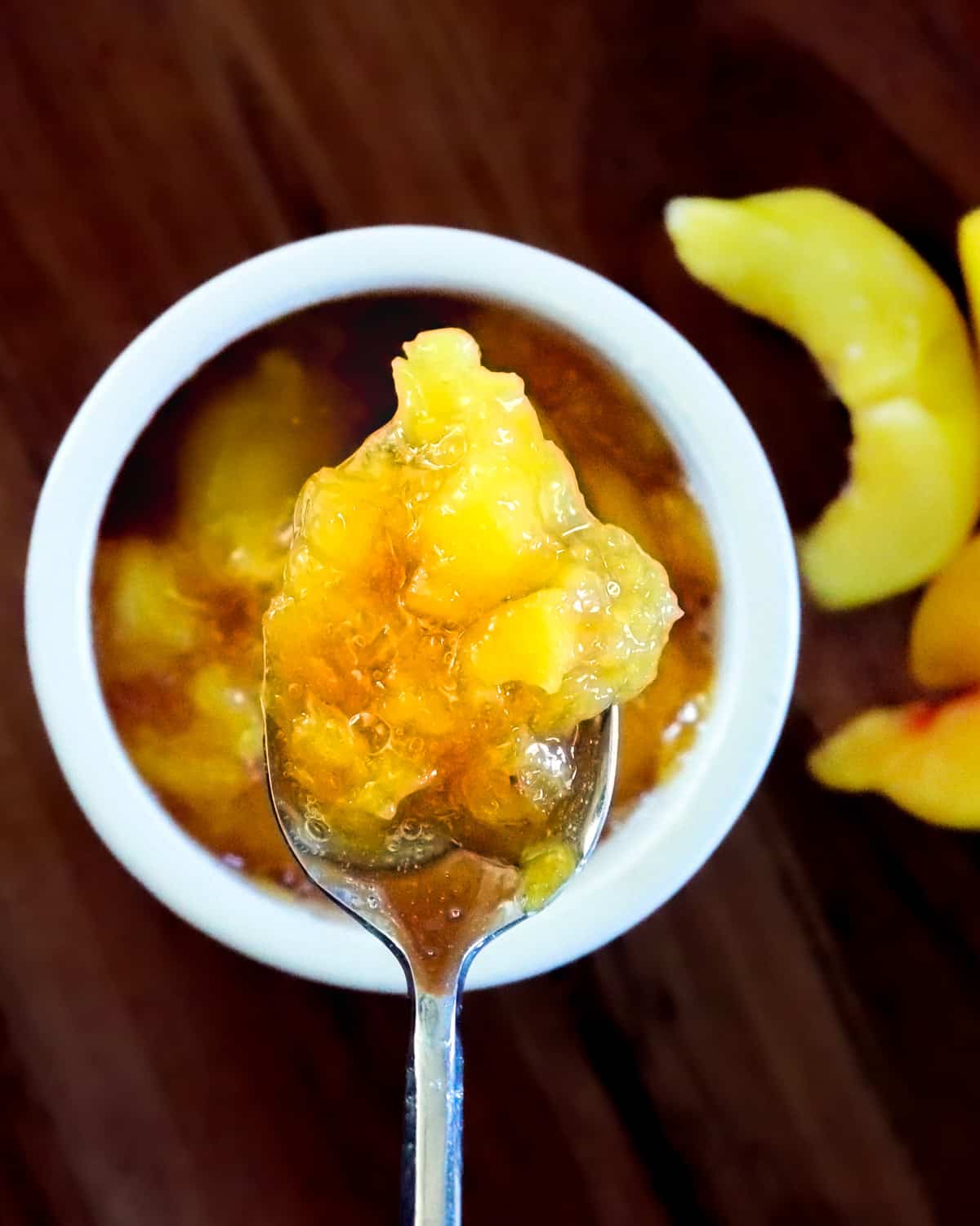 A spoon holding peach compote close to the camera.