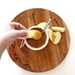 Hand dipping apple slice into curd.