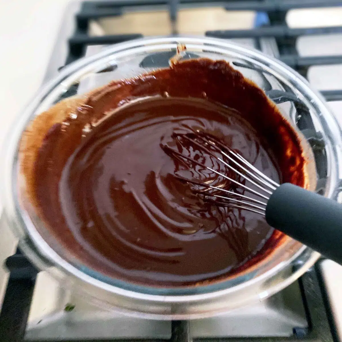 A whisk laying on the side of the bowl with the chocolate fully incorporated.