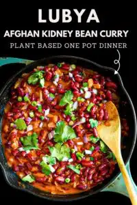 Picture of lubya in a skillet garnished with cilantro and a wooden spoon.