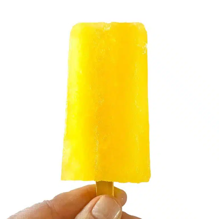 A hand holding up a bright yellow lemonade popsicle.