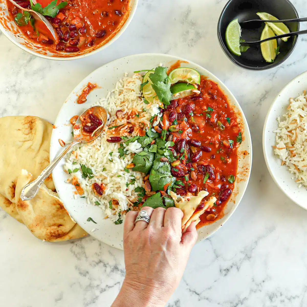 Hand dipping nann into a plate filed with garnished lubya and rice.