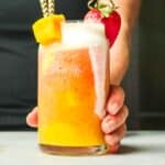 Hand holding a glass of banana strawberry mango smoothie that has been mixed together.