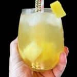 Hand holding up the pineapple passionfruit refresher against a black background.
