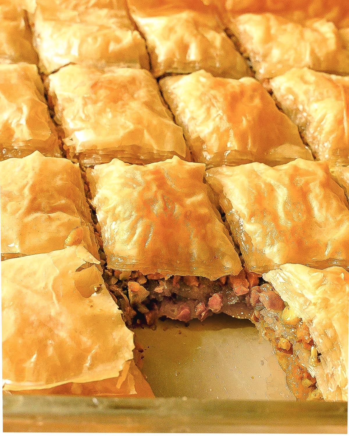 Pistachio baklava in a tray with one piece missing.
