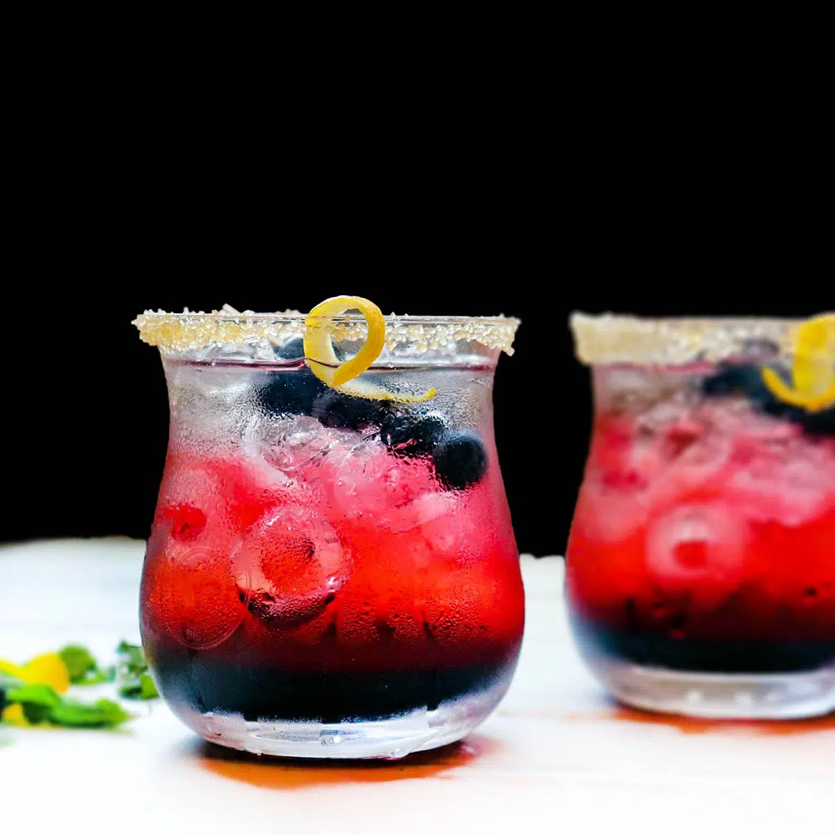 Blueberry and gin cocktail. Glass garnished with sugar and lemon curl.