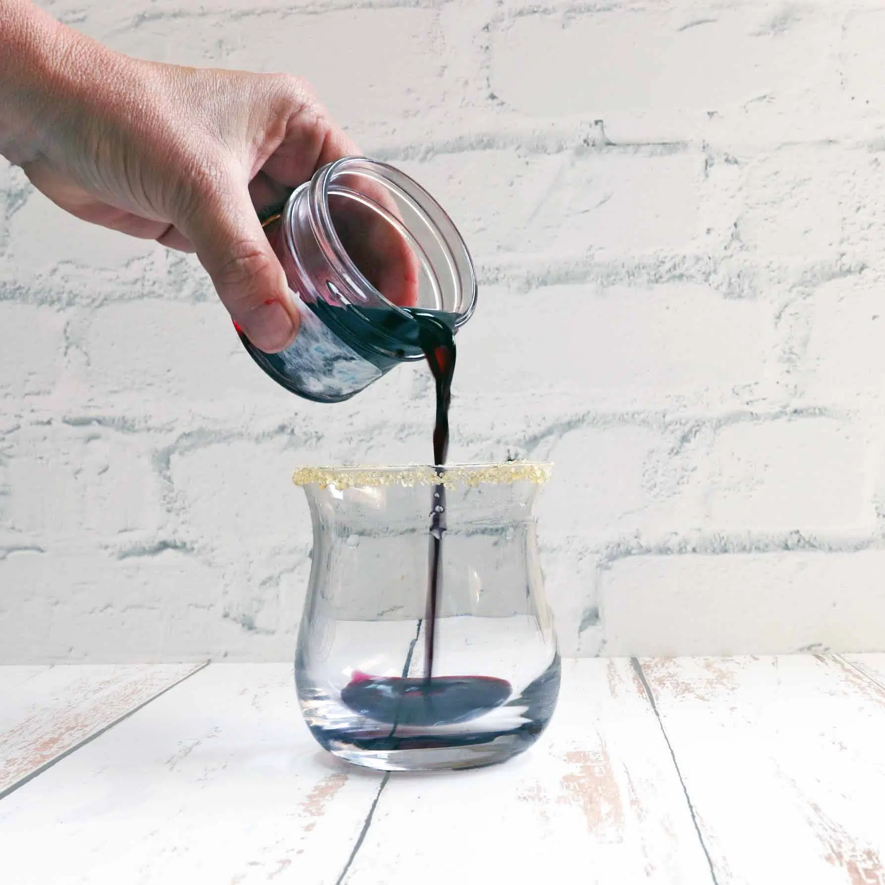 Pouring blueberry simple syrup into gin cocktail glass.
