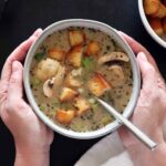 Two hand cupping a bowl of creamy mushroom soup.
