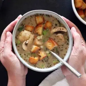 Two hand cupping a bowl of creamy mushroom soup.