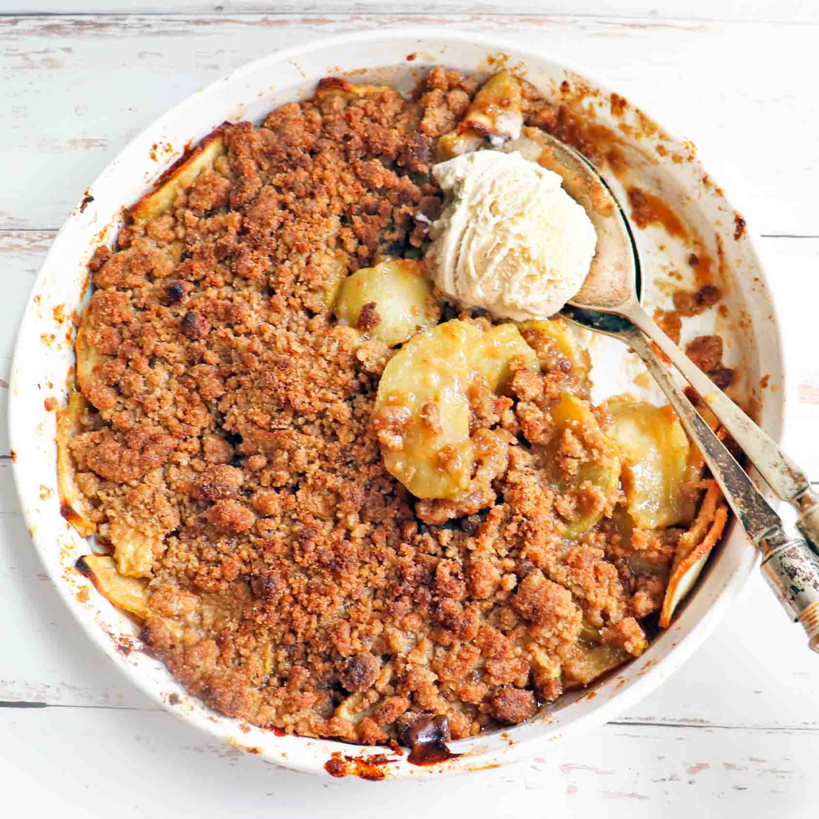 Vegan apple crumble with a scoop of ice cream and two spoons.