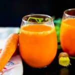 Carrot ginger juice in a juice glass with a knob of ginger next to it.