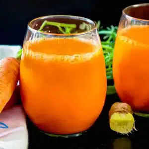 Carrot ginger juice in a class with a nob of ginger near it.