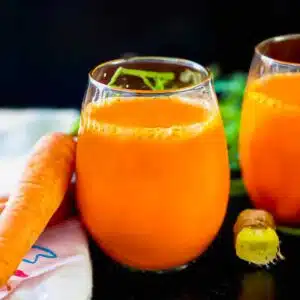 Carrot ginger juice in a juice glass with a knob of ginger next to it.
