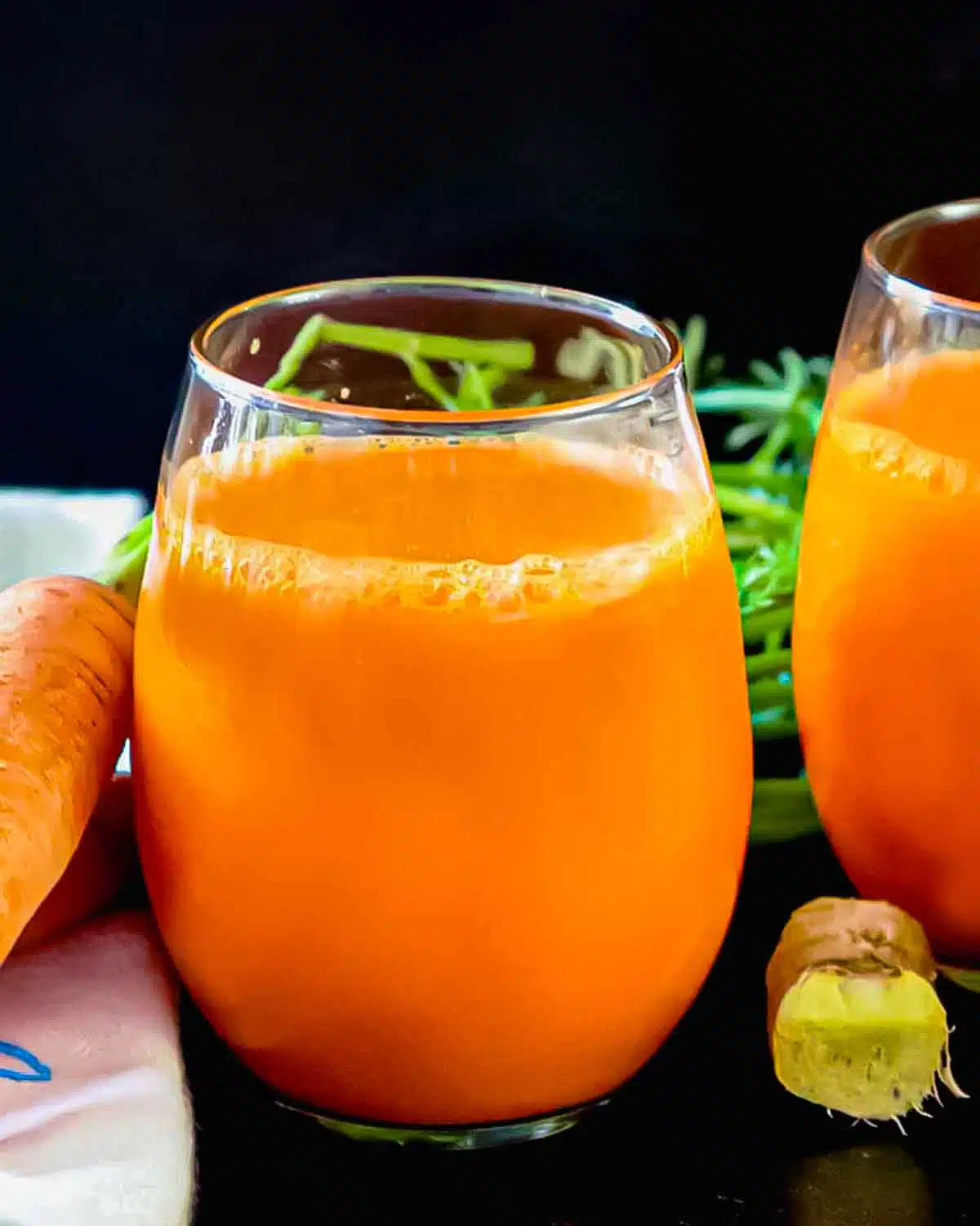 Carrot ginger juice in a class with a nob of ginger near it. 