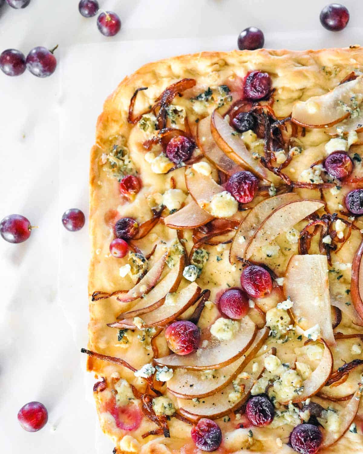 Pear, red grape and blue cheese focaccia bread with red grapes scattered around.