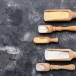 Five wood scoops filled with different kinds of flour.