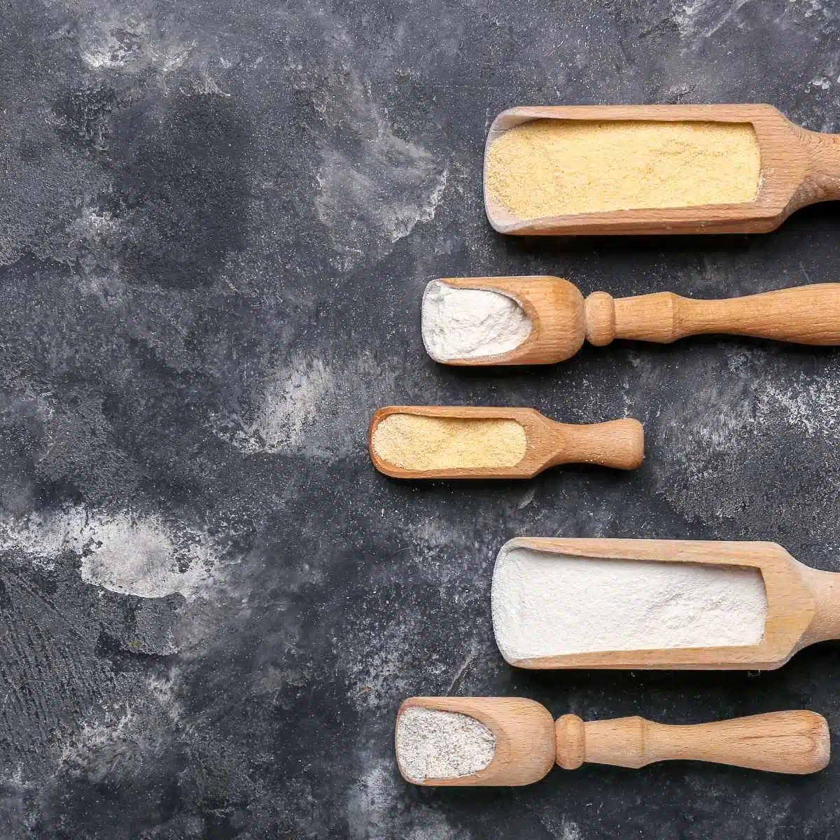 Five wood scoops filled with different kinds of flour.
