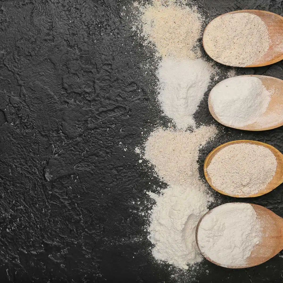 Four different wooden spoons filled with flours.