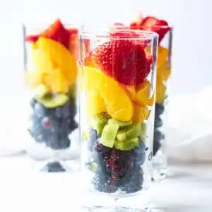 Three glasses filled with rainbow arranged fruit.
