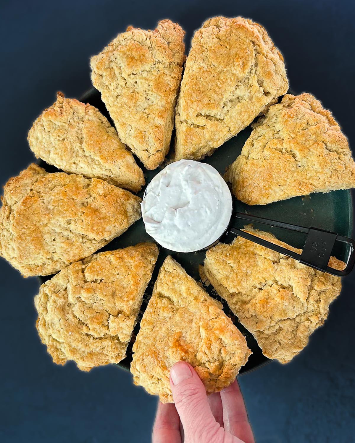 Hand reaching for a vegan scone with vegan clotted cream in the center.
