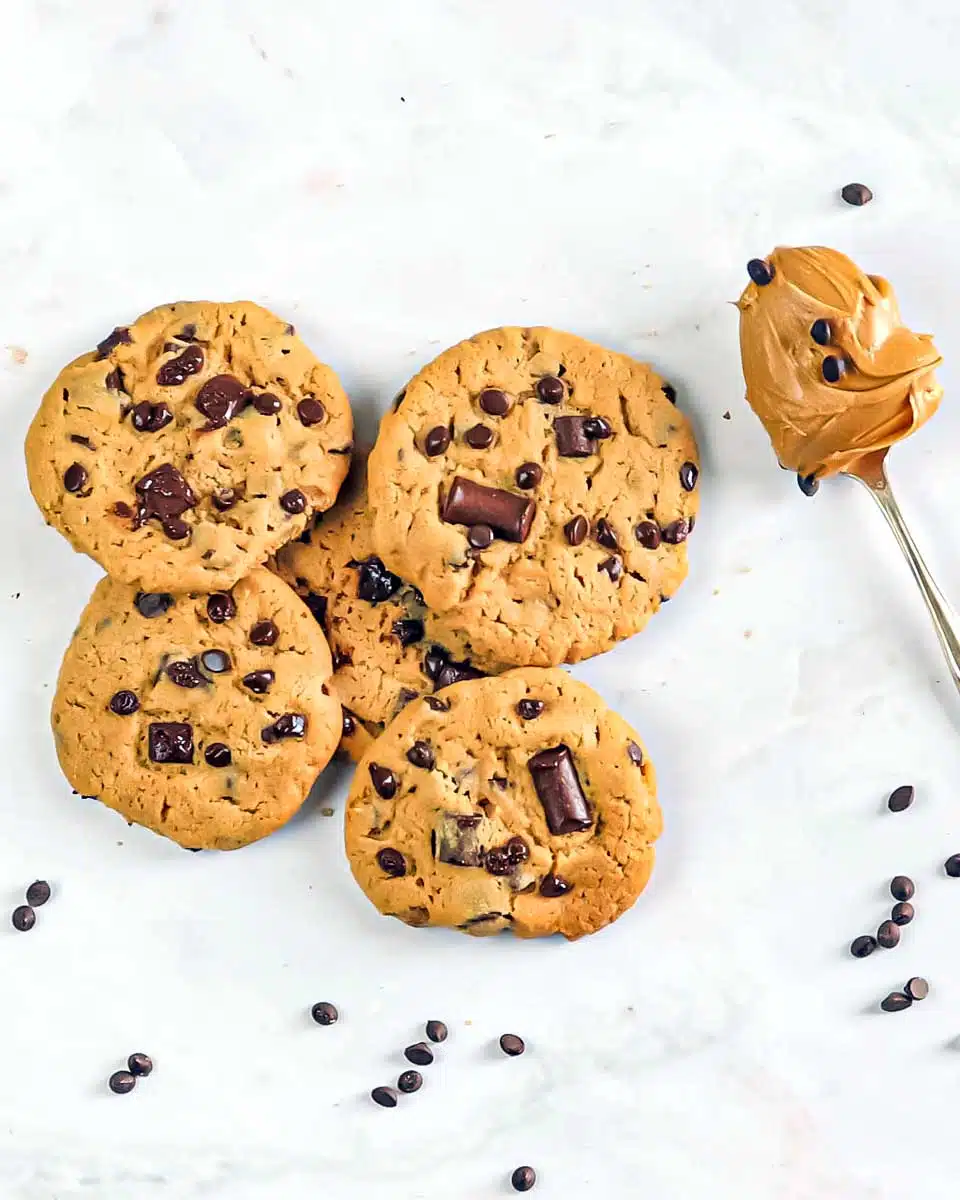 A scattering of cookies and a spoon filled with peanut butter.