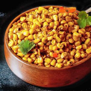 A bowl filled with blacked corn and garnished with cilantro leaves.