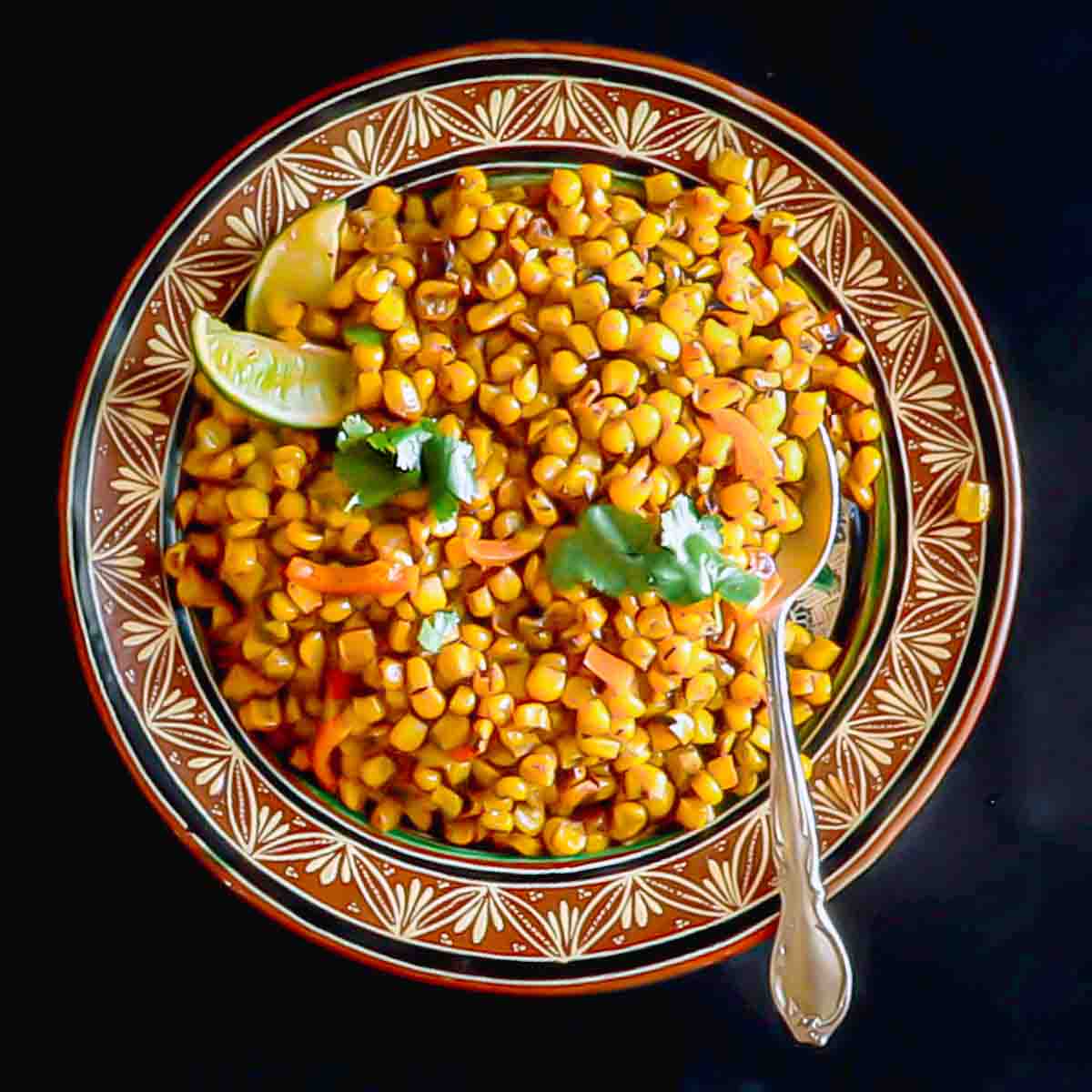 Blackened corn in a bowl with a spoon.