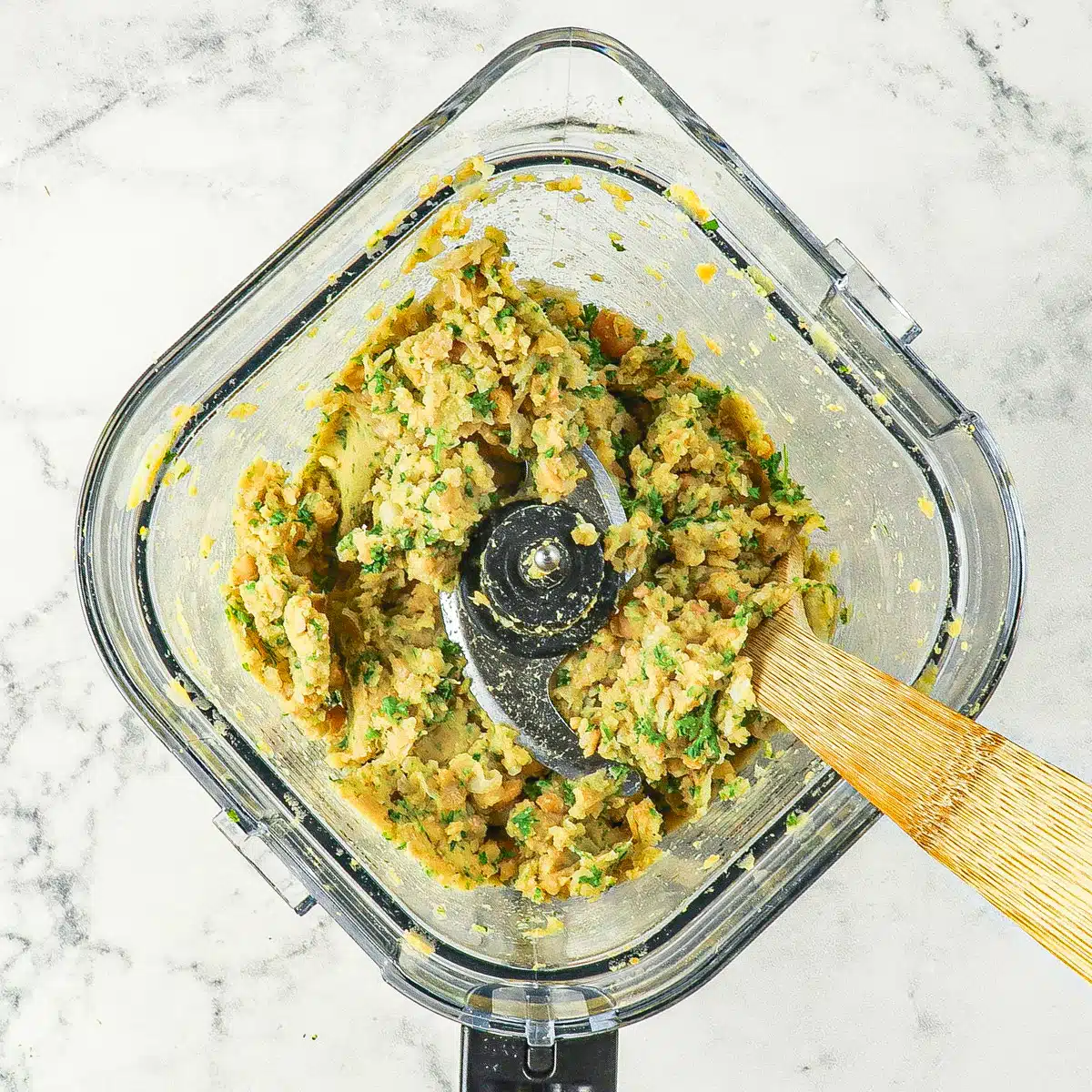 Blended falafel in a food processor with a wooden spoon.