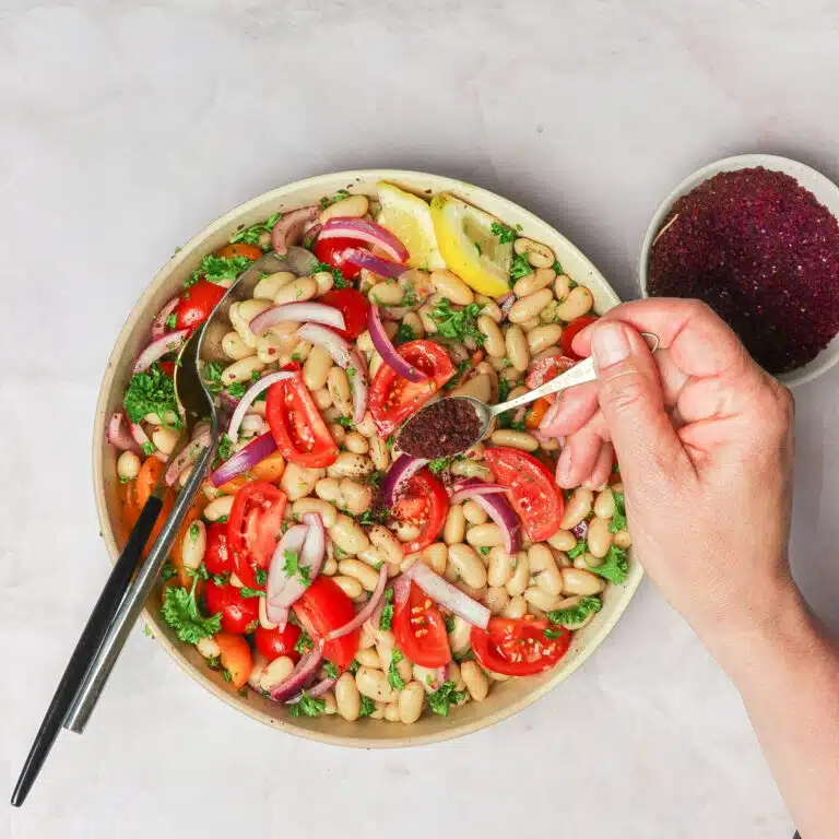 Hand sprinkling sumac on the salad.