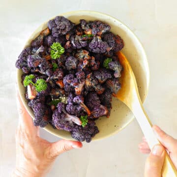 Roasted cauliflower in a bowl, cupped with two hands and a wooden spoon.