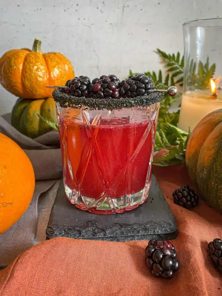 Cocktail in a whiskey glass garnished with blackberries.