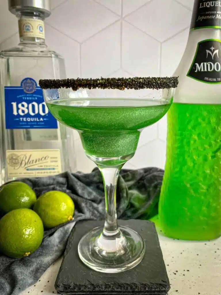 Margarita in a glass surrounded by limes.