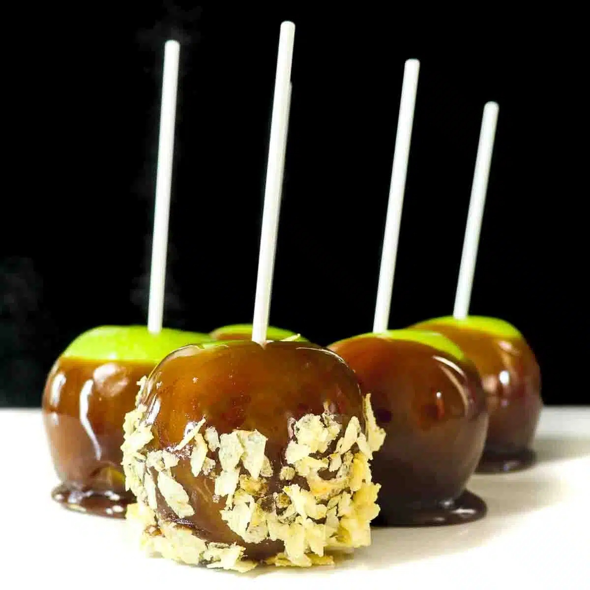 Five caramel apples. The apple in the forefront has potato chips in the caramel.