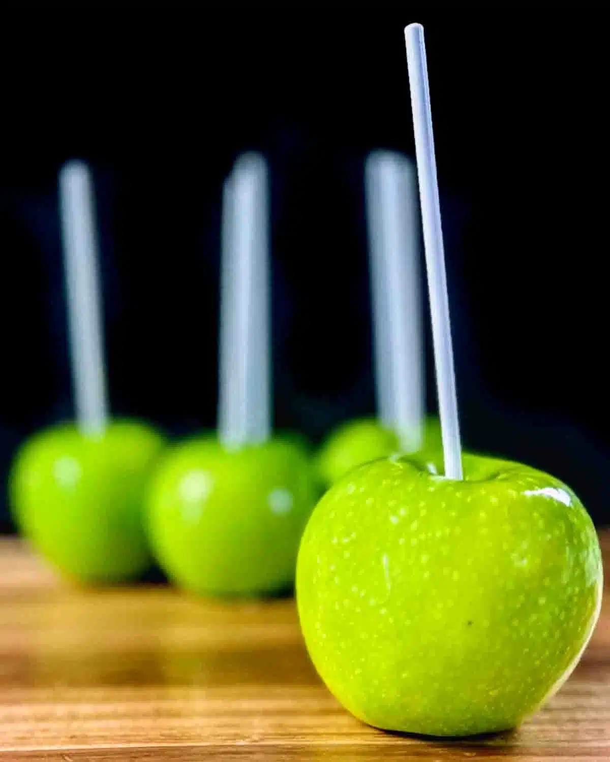 Several green apples with sticks. The apple in the front is in focus.