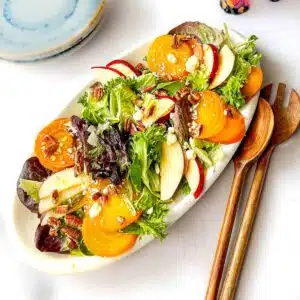 Salad on a long platter with serving spoons next to it.