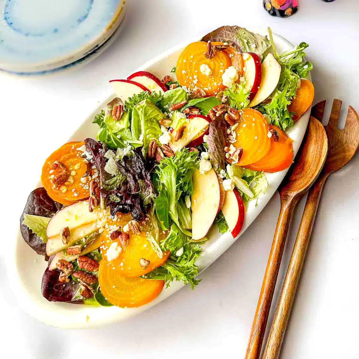 Salad on a long platter with serving spoons next to it. 